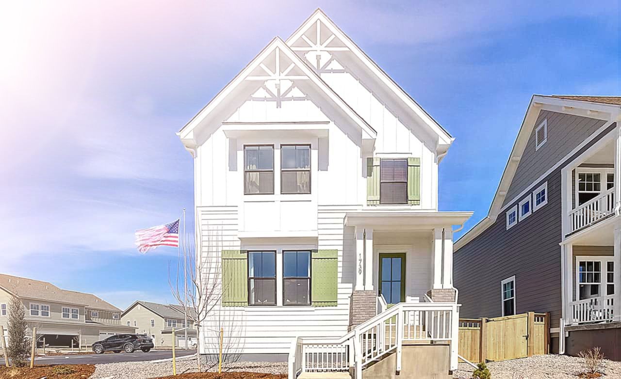 Modern white house with green shutters and gables in Westerly community. American flag in front yard, bright blue sky.