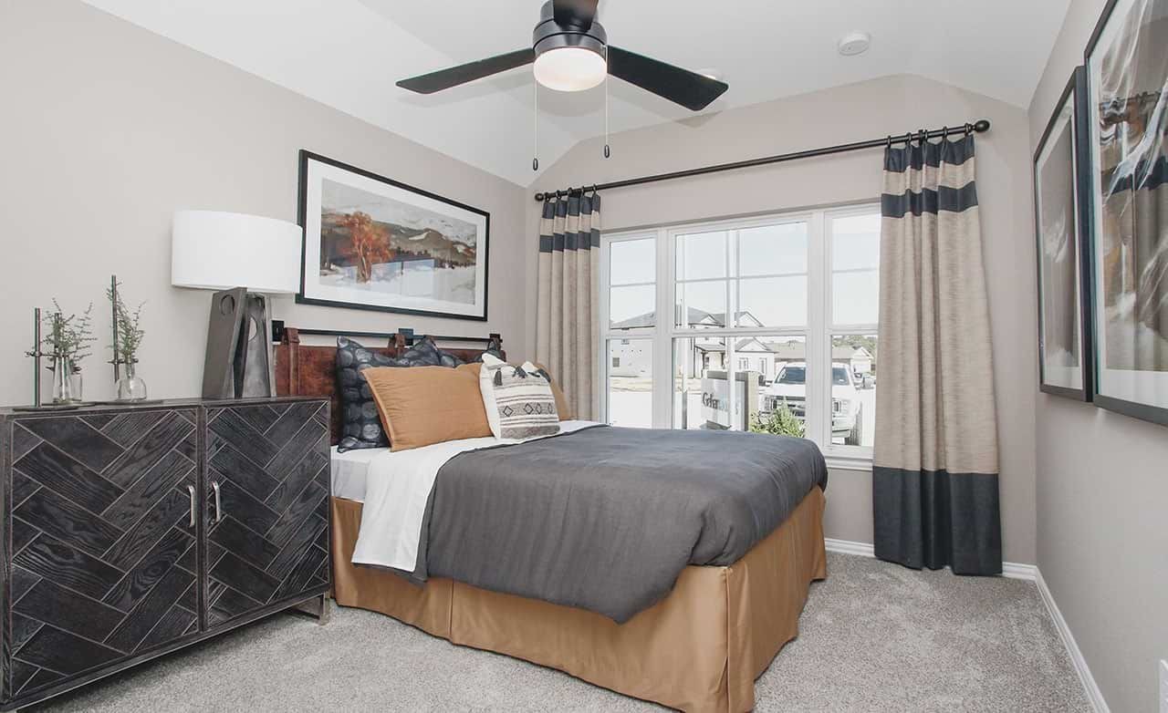 Elegant bedroom with modern décor, large window, stylish fan, and unique dresser in Cypress Green community.