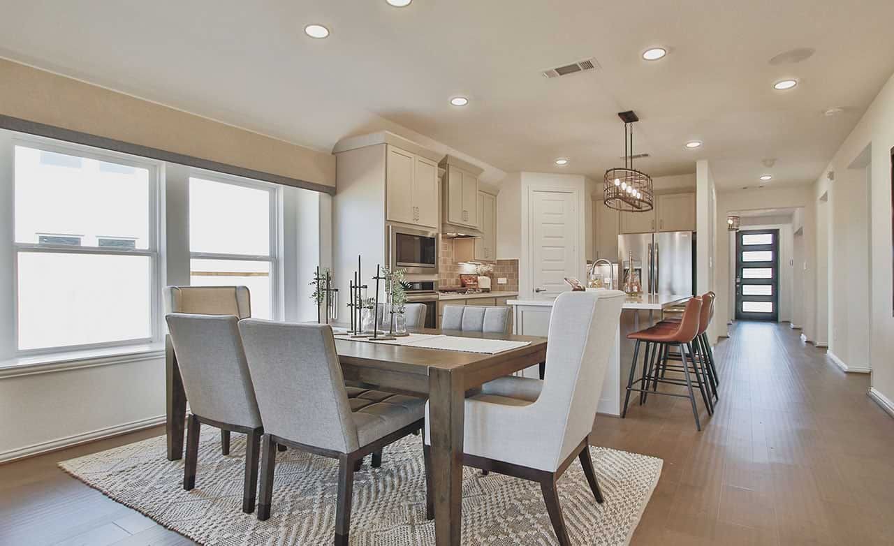 Modern dining area with beige chairs, wooden table, open kitchen, and sleek flooring in Cypress Green community.
