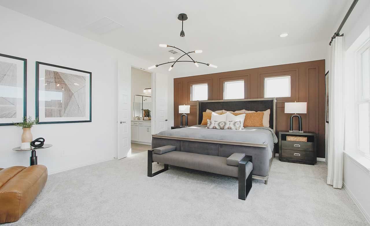 Modern bedroom in Cypress Green community with wood accent wall, chic chandelier, and plush carpeting.