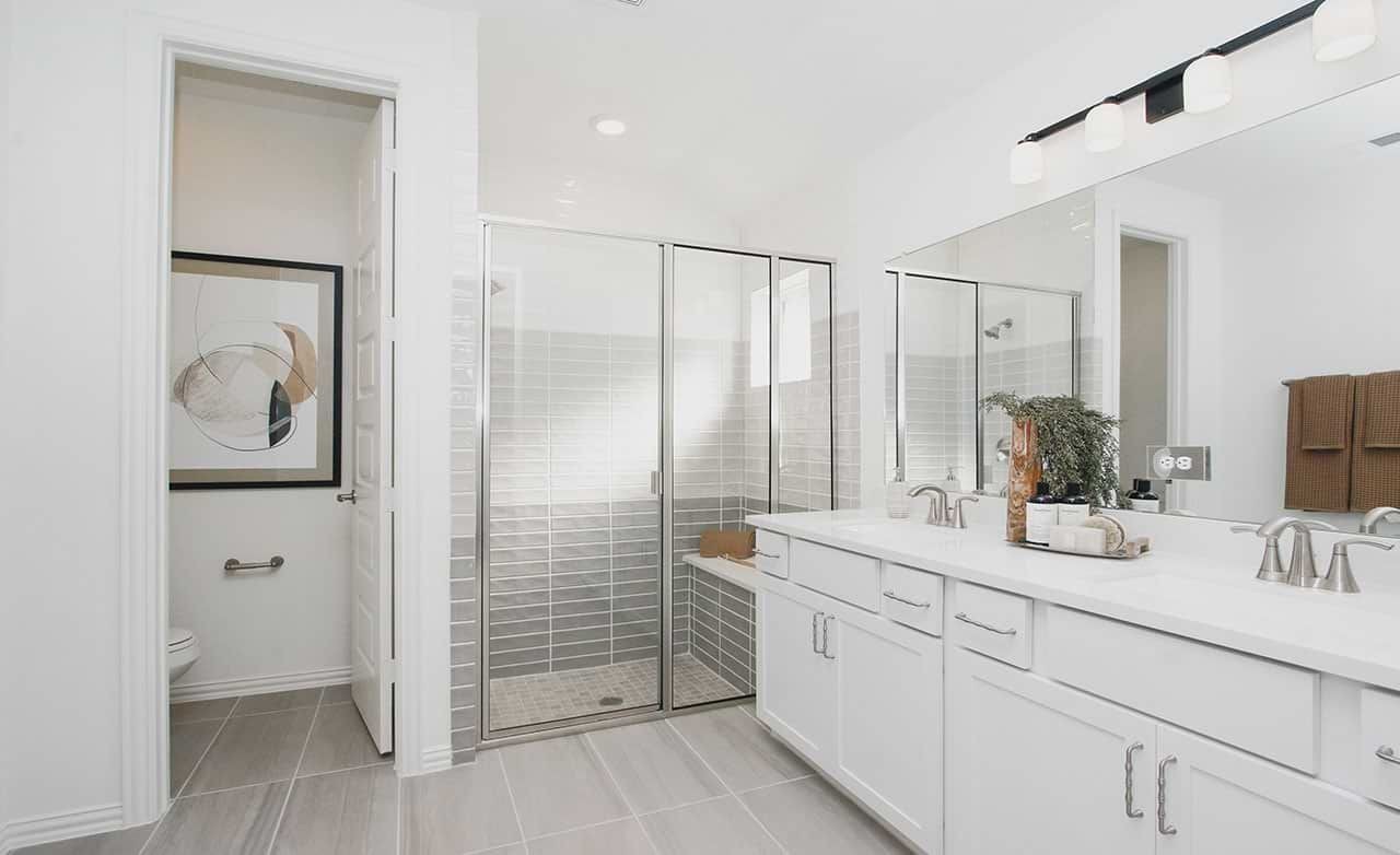 Modern bathroom with dual sinks, glass shower, and abstract art in Cypress Green. Neutral tones, abundant light.