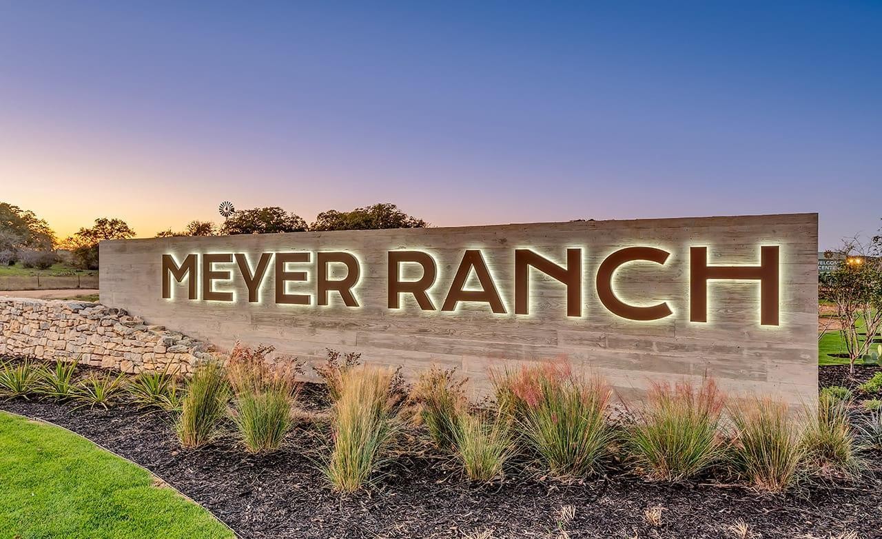 Illuminated Meyer Ranch sign on stone wall at sunset, lush landscaping, Texas.