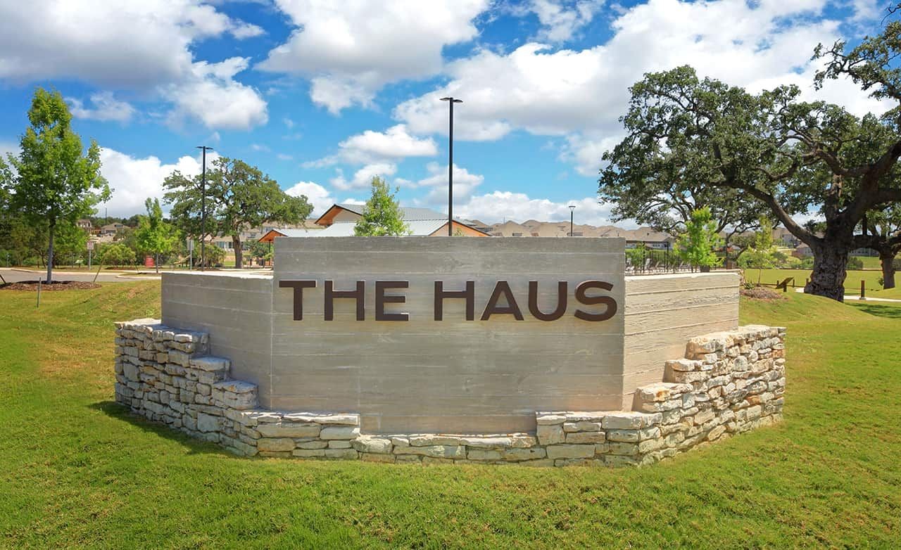 Stone sign reading "THE HAUS" in Meyer Ranch community, Texas, surrounded by lush greenery and clear blue sky.