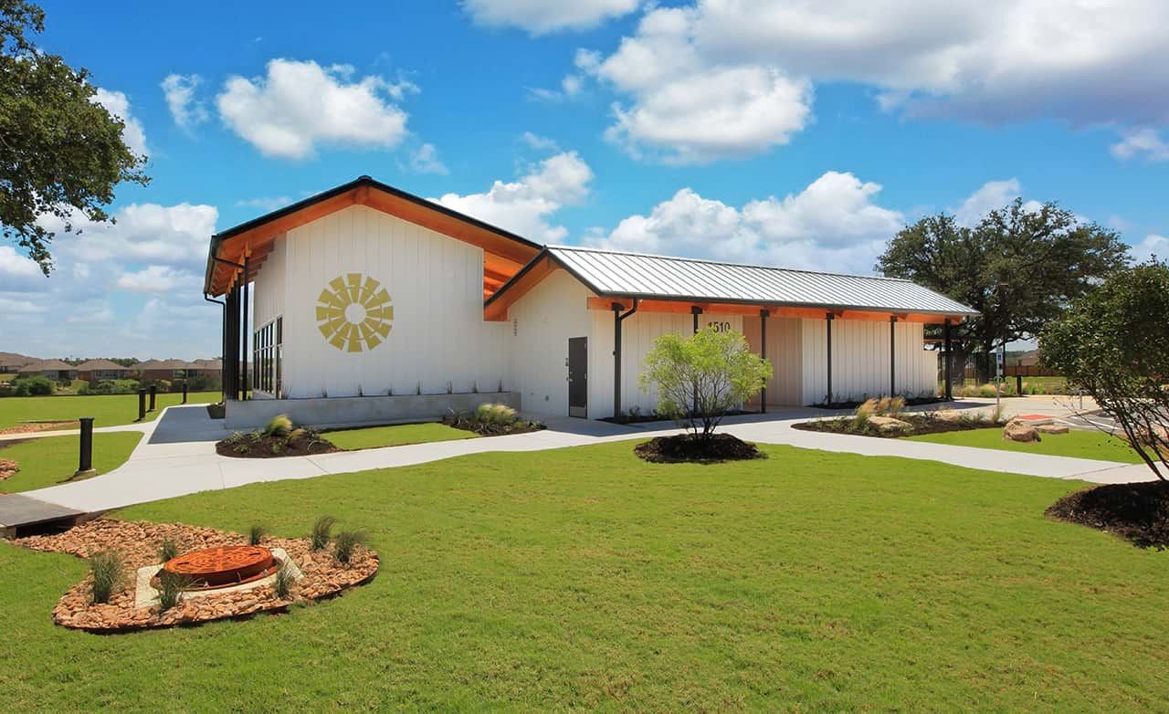 Modern white building at Meyer Ranch, Texas, with metal roof, wooden accents, manicured lawns, and blue sky.