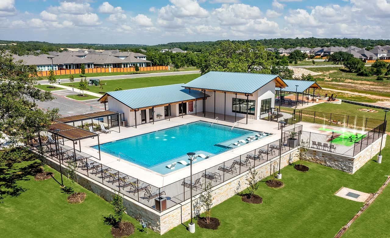Modern clubhouse with pool, metal roof, and expansive lawn in Meyer Ranch, Texas community.