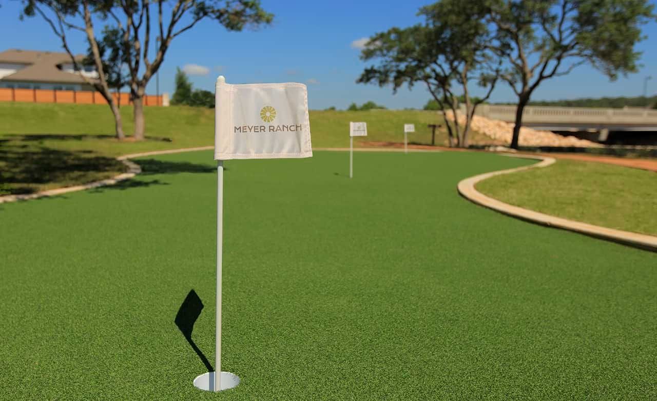 Green putting course at Meyer Ranch with flags, lush trees, and clear sky in suburban setting.