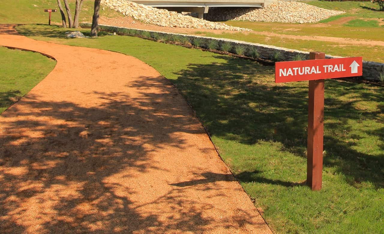 Winding natural trail with sign, surrounded by greenery at Meyer Ranch. Bridge and stone wall in background.