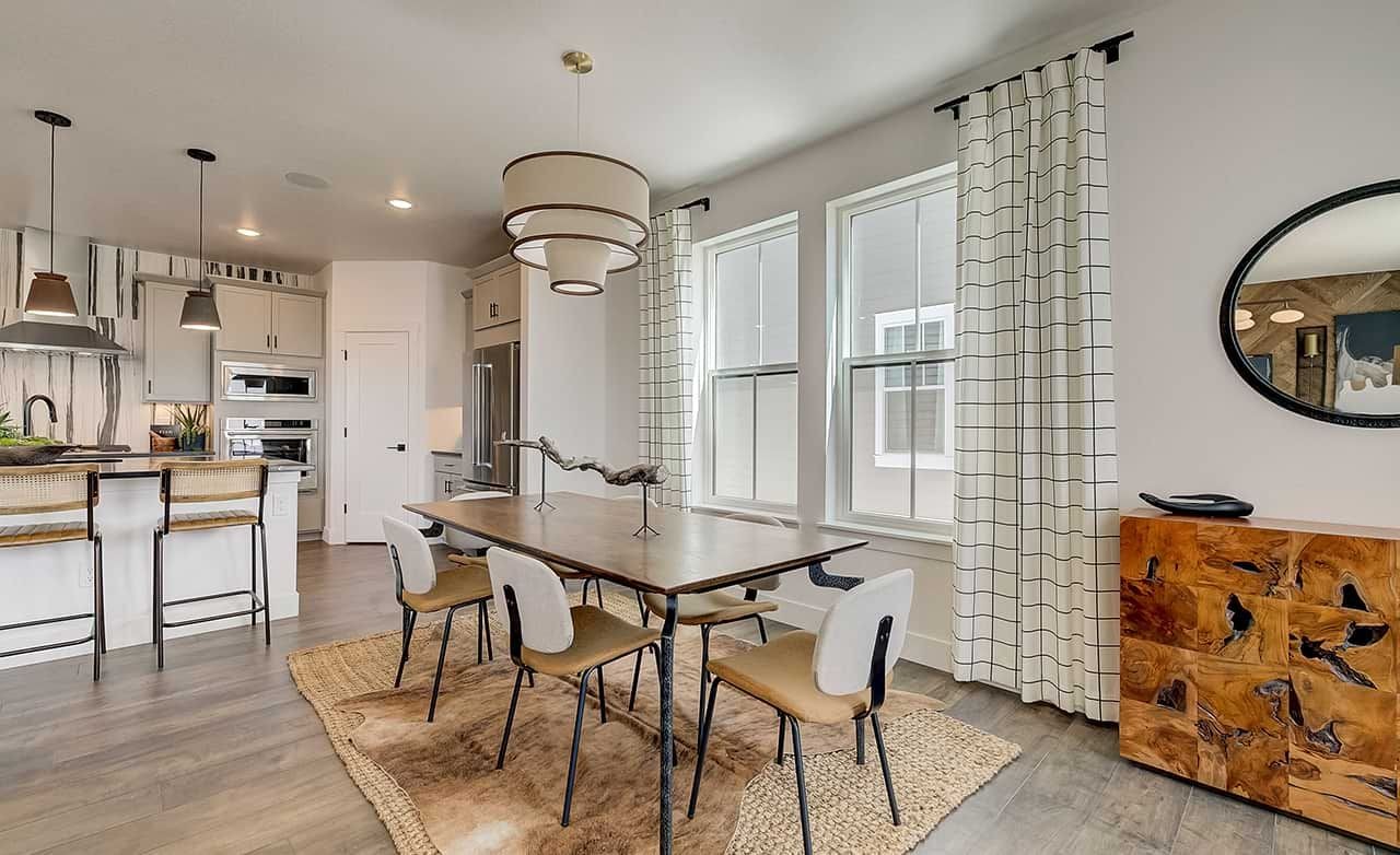 Elegant dining room with wood table, modern kitchen, pendant lights, and natural light in Westerly community.