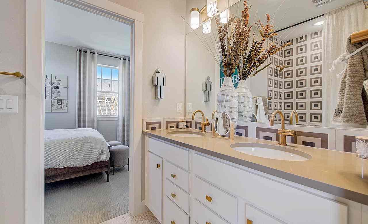 Modern bathroom with dual sinks, gold fixtures, geometric tile in Westerly community home.