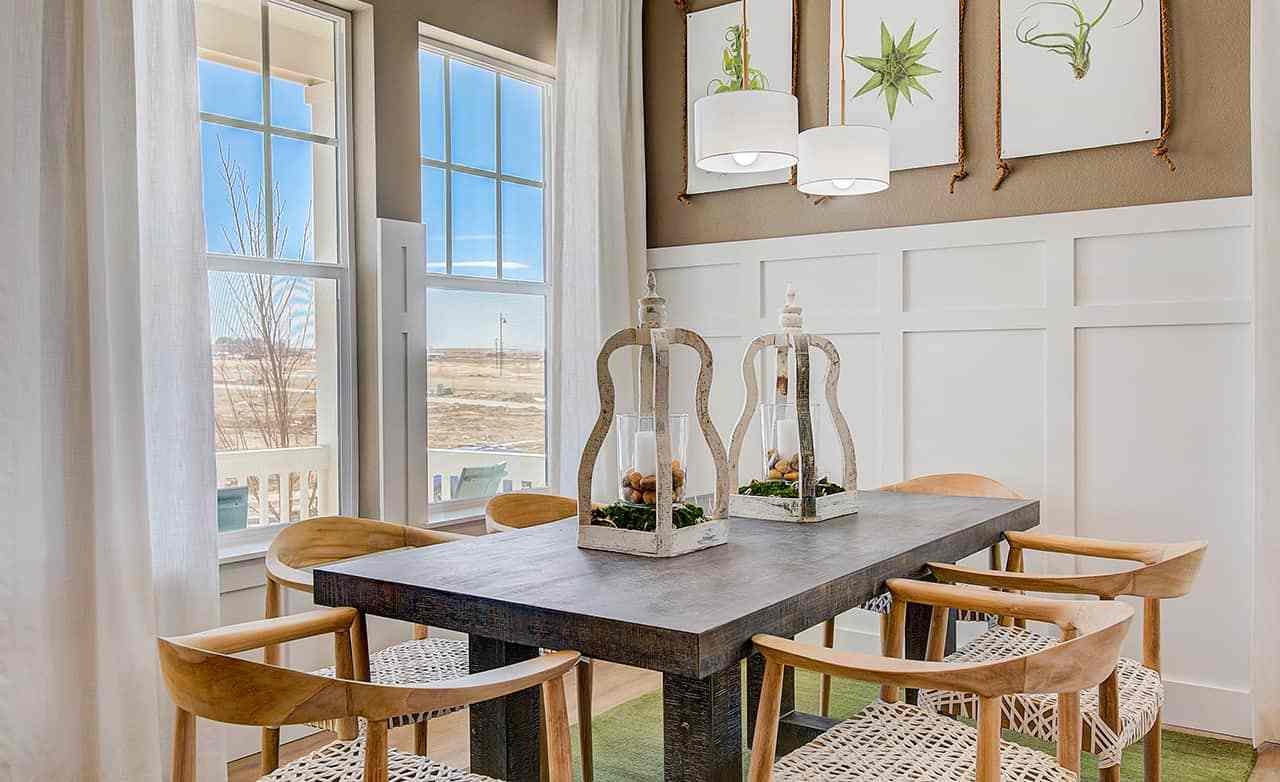Elegant dining room with large windows, wood table, wicker chairs, and modern decor in Westerly community.