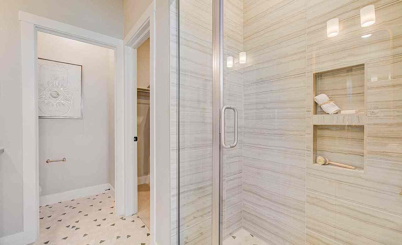 Luxurious marble shower with glass door, inset shelves, modern mosaic floor, Westerly location.