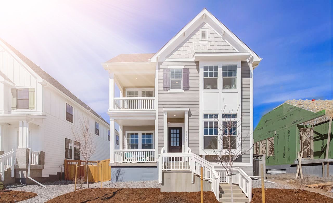 Two-story house with porch, gable roof, and large windows in sunny Westerly community near construction site.