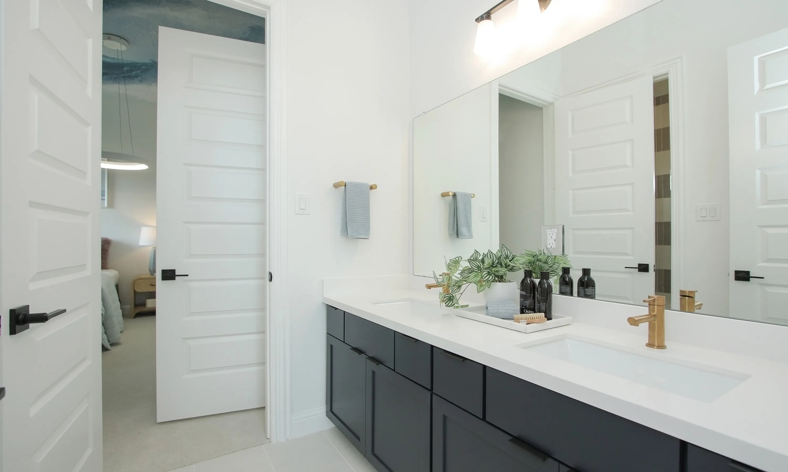 Modern Bathroom with Dual Sinks in Coastal Point Community Modern bathroom with dual sinks, black cabinets, gold fixtures, large mirror, and white doors. Coastal Point community.